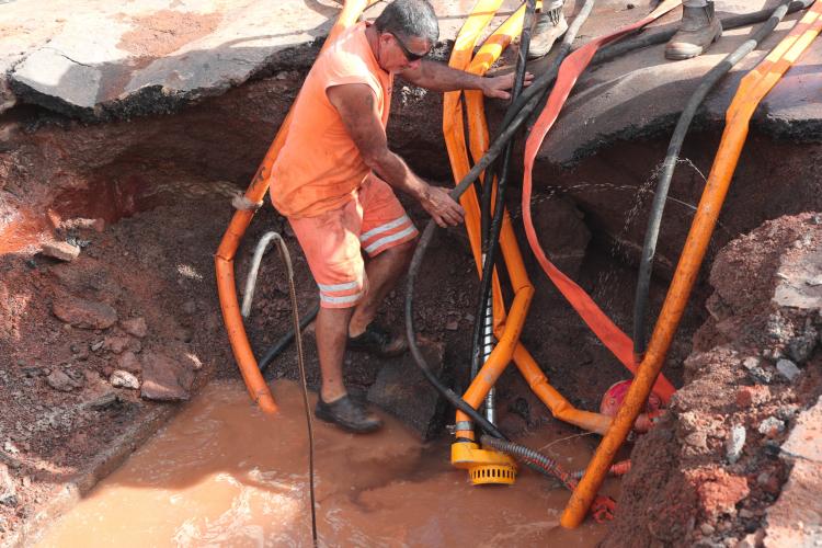 Servidor público drena água da valeta antes de um serviço emergencial na rede pública de abastecimento.