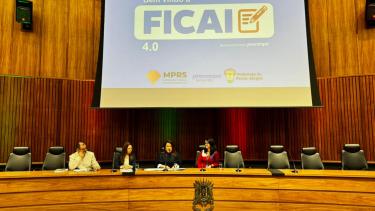 Slides de apresentação do relatório da Ficai ao fundo e quatro pessoas sentadas